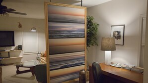 Una habitación con escritorio, silla, televisión y un cuadro grande.