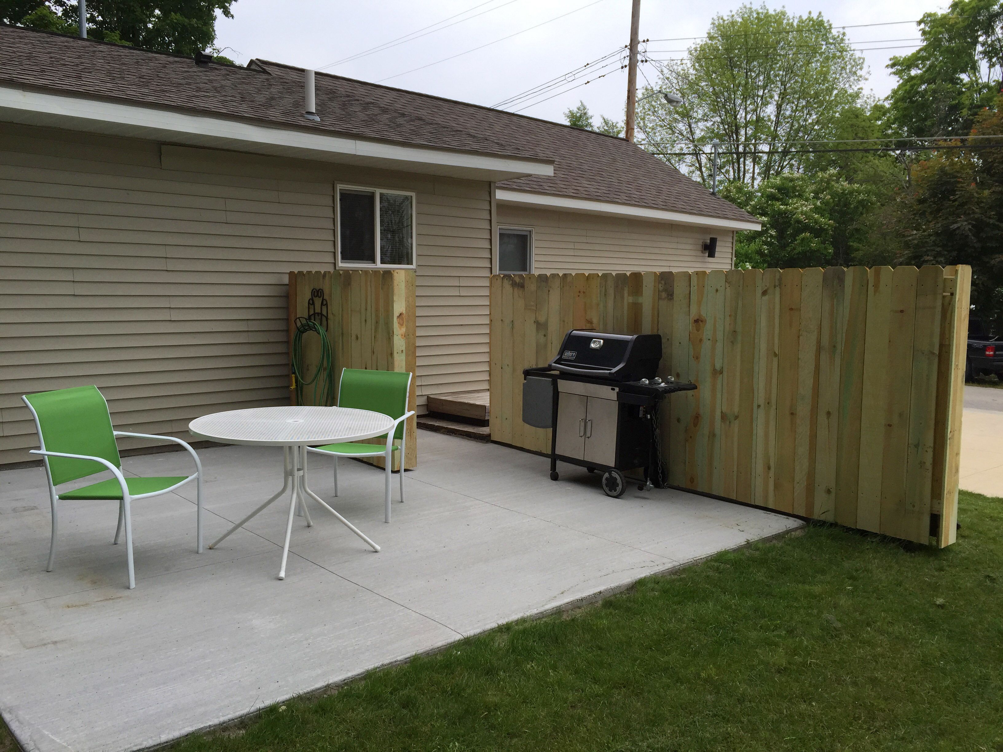 A patio with a grill, two chairs, and a table.