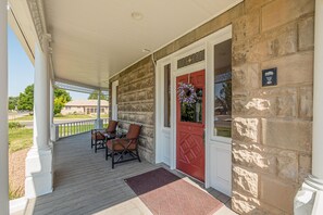A covered porch with a stone wall, a red door, and two chairs. - Sagebrush V: Pet Friendly Historical Stay (Fruita)