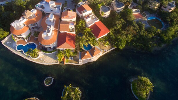 Luftaufnahme eines Resorts mit mehreren Gebäuden, einem zentralen Pool und umliegenden Palmen.