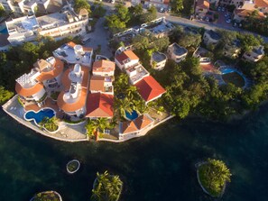 An aerial view of a resort with multiple buildings, a central pool, and surrounding palm trees.