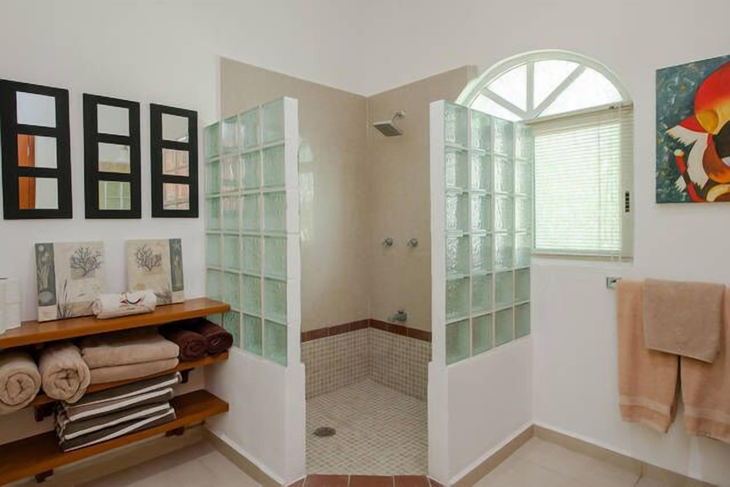 A bathroom with a shower, a glass door, a towel rack, and a shelf with towels.
