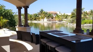 Eine Terrasse mit Tisch und Stühlen mit Blick auf ein Gewässer, Palmen und ein Gebäude im Hintergrund.