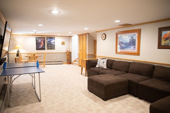 A living room with a ping pong table, a brown sectional sofa, and a wooden cabinet.