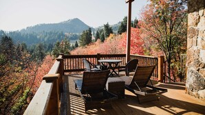 Eine Holzterrasse mit Korbmöbeln und einer Steinmauer, mit Blick auf eine bewaldete Berglandschaft.