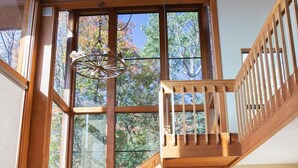 Ein geräumiges Zimmer mit großen Fenstern, einer Holztreppe und einer gemütlichen Sitzecke mit gemusterten Kissen.