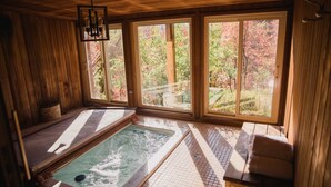 Ein Spa-Raum mit Holzboden, einer Whirlwanne, großen Fenstern und einer Sitzbank.