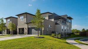 A modern multi-story residential building with a flat roof, large windows, and a well-maintained lawn. - Townhome with Loft & Contemporary Flair!  Convenient & Straight Route to A&M! (College Station)