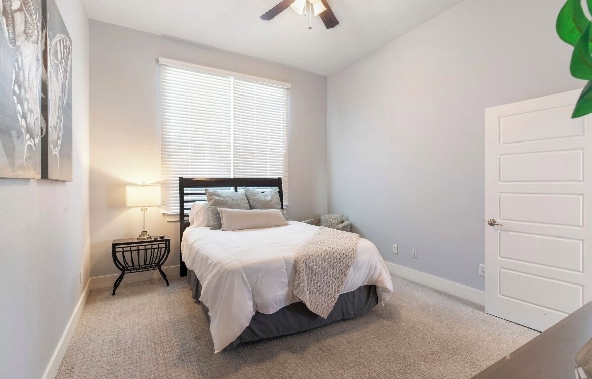 Une chambre à coucher avec un lit, une table de chevet, une lampe, une fenêtre et une porte.