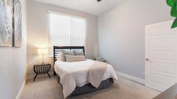 Une chambre à coucher avec un lit, une table de chevet, une lampe, une fenêtre et une porte.