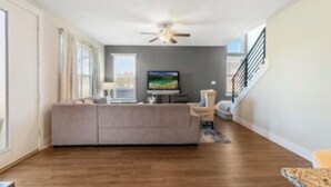 A modern living room with a large sofa, a flat-screen TV, and a ceiling fan. - Townhome with Loft & Contemporary Flair!  Convenient & Straight Route to A&M! (College Station)