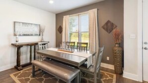A dining area with a table, chairs, and a bench. There is a window with curtains, a vase with branches, and a painting on the wall. - Townhome with Loft & Contemporary Flair!  Convenient & Straight Route to A&M! (College Station)