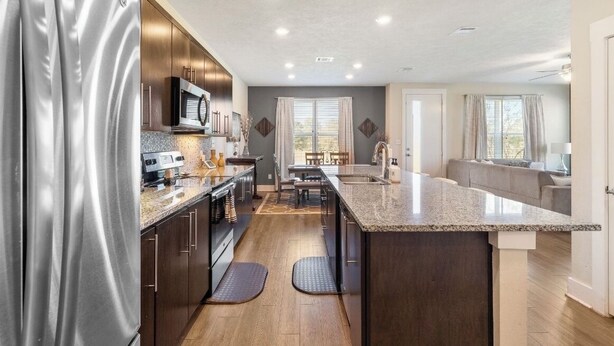 A modern kitchen with dark wood cabinets, stainless steel appliances, and a granite countertop. - Townhome with Loft & Contemporary Flair!  Convenient & Straight Route to A&M! (College Station)