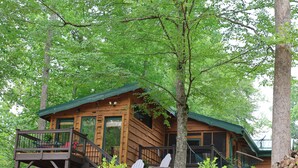 Une cabane en bois dotée d’une terrasse, de deux fauteuils Adirondack et d’un hamac.