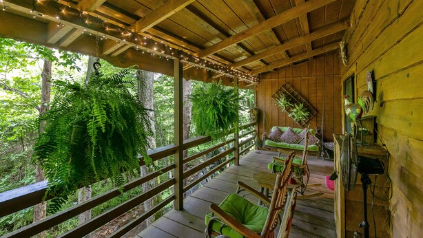 Une terrasse en bois avec une rambarde, des chaises rembourrées vertes et un banc en bois.