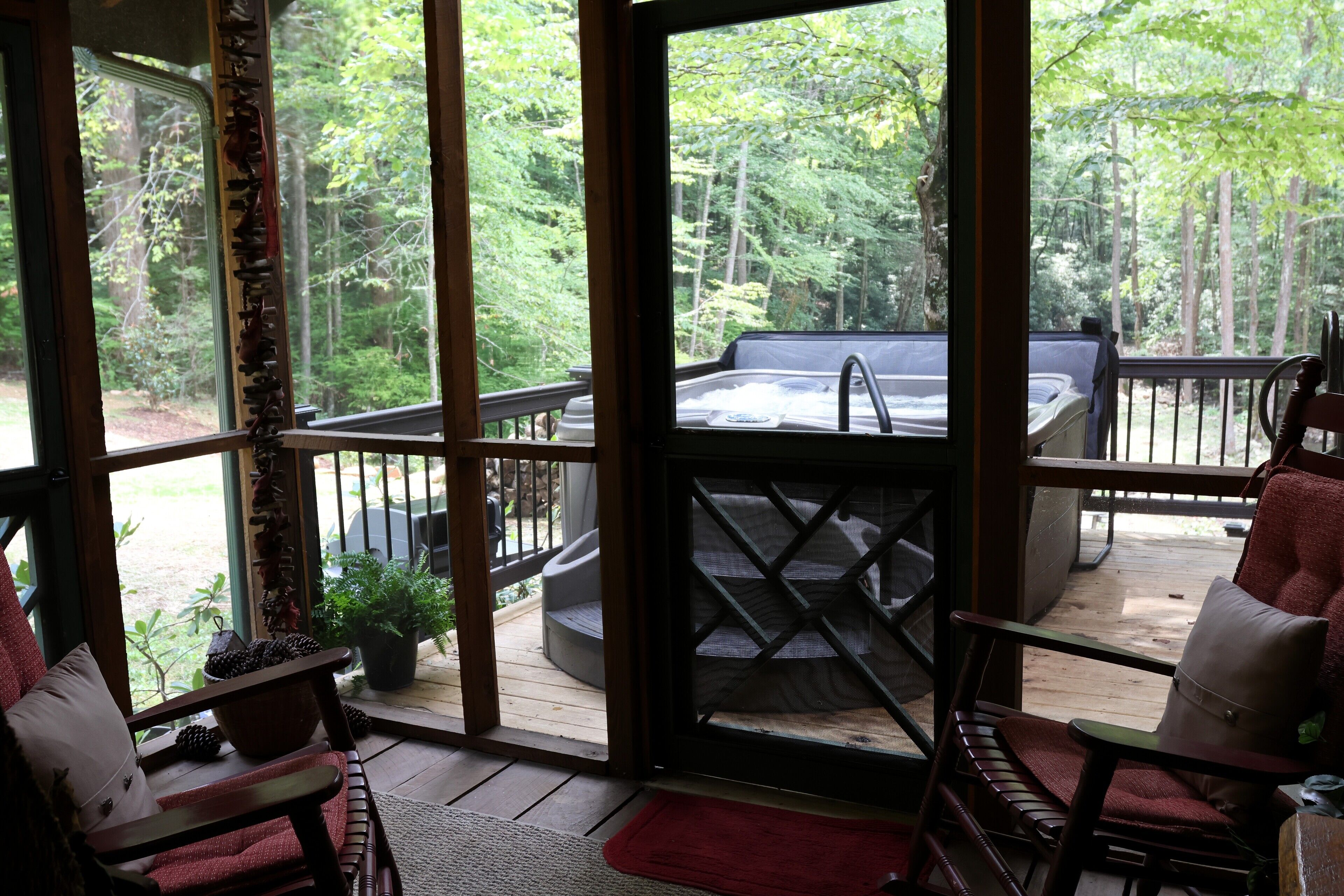 Una terraza de madera con un jacuzzi, mobiliario exterior y vistas a un bosque.