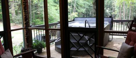 Una terraza de madera con un jacuzzi, mobiliario exterior y vistas a un bosque.