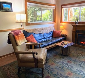 A cozy living room with a leather sofa, a wooden chair, a small table with drinks, and a fireplace.