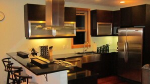 Una cocina moderna con armarios oscuros, electrodomésticos de acero inoxidable y una isla central con taburetes de bar.
