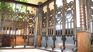 Una reja de hierro forjado con diseños intrincados, un pilar de madera y una planta en maceta al fondo.