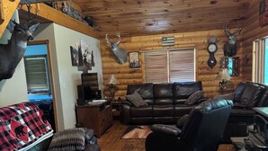 A cozy cabin interior with a wooden ceiling, a leather sofa, a fireplace, and deer antlers on the walls. - 4 bedroom, Secluded 13 Acres on Bennetts Branch of the Sinnemahoning Creek.  (Benezette)
