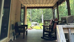 A covered wooden deck with string lights, outdoor furniture, and a view of the forest. - 4 bedroom, Secluded 13 Acres on Bennetts Branch of the Sinnemahoning Creek.  (Benezette)