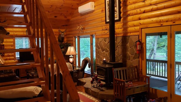 A log cabin interior with a stone fireplace, wooden shelves, and a cozy seating area. - 4 bedroom, Secluded 13 Acres on Bennetts Branch of the Sinnemahoning Creek.  (Benezette)