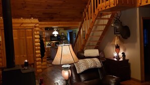 A cozy cabin interior with a wooden staircase, a fireplace, a leather sofa, and a dining area. - 4 bedroom, Secluded 13 Acres on Bennetts Branch of the Sinnemahoning Creek.  (Benezette)