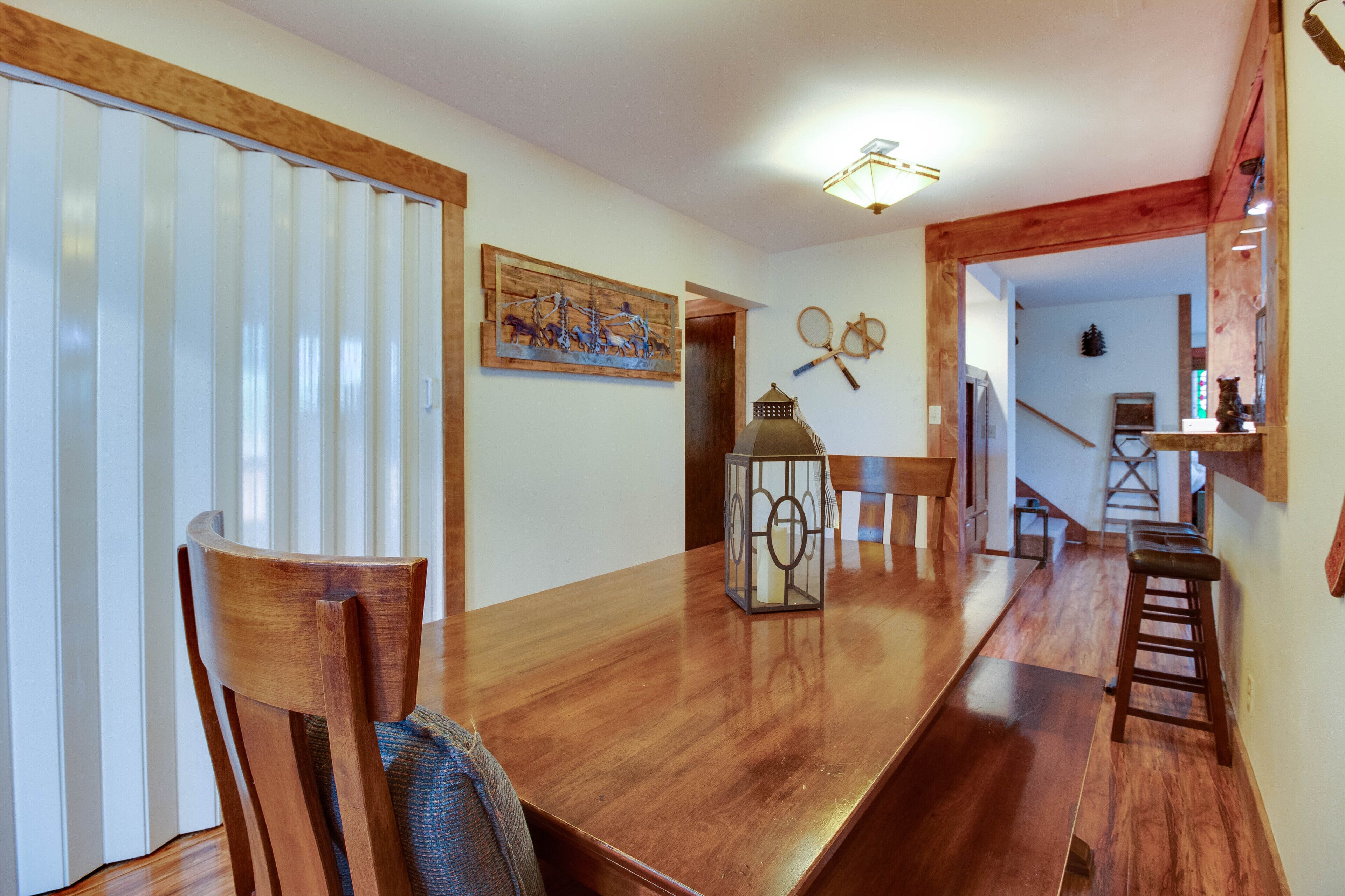 Un comedor con mesa de madera, sillas y un farol. Una escalera conduce a otra habitación.