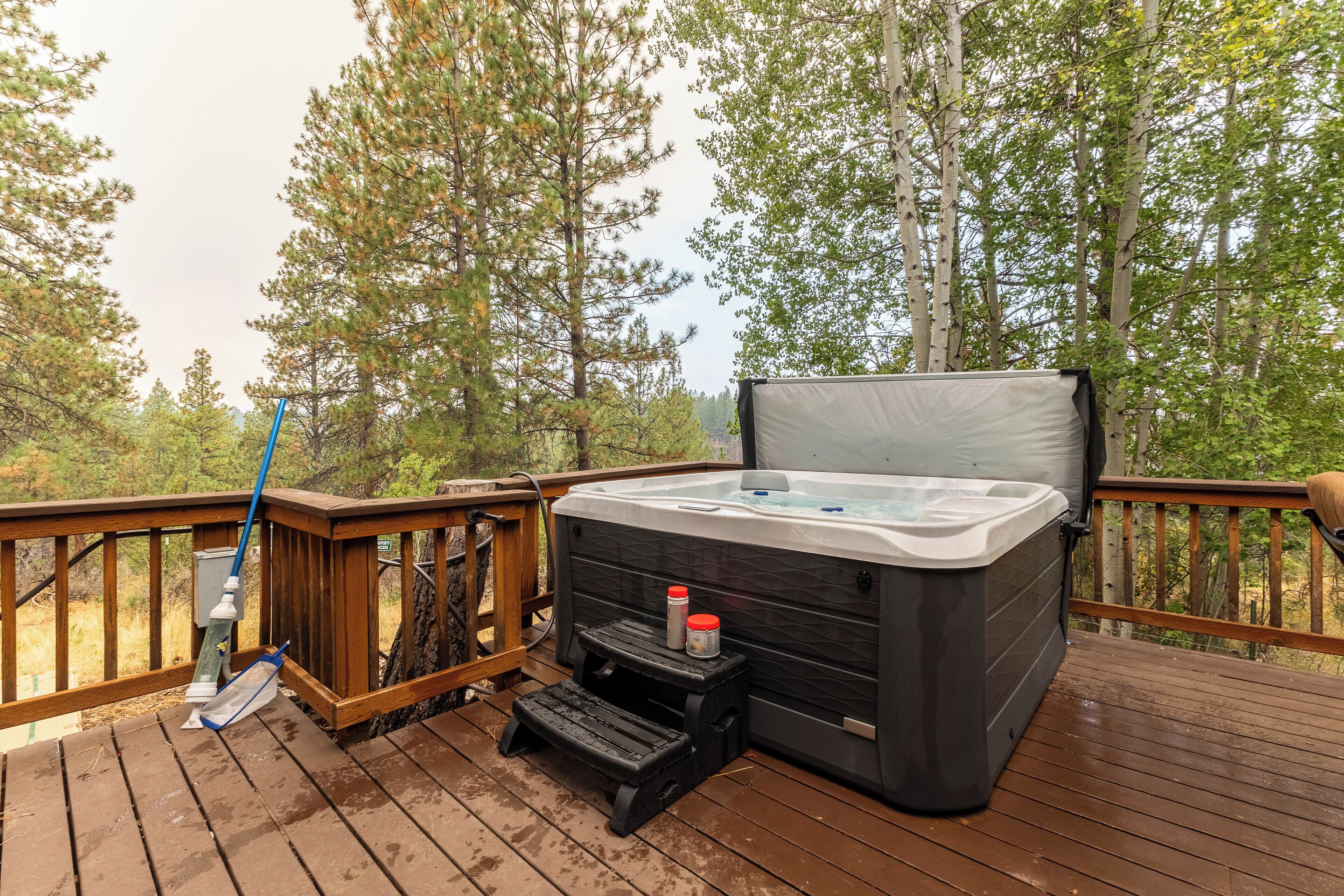 A hot tub on a wooden deck with a step stool and a bottle of sunscreen.