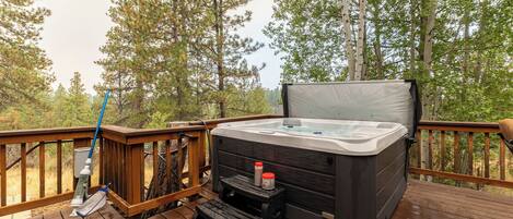 A hot tub on a wooden deck with a step stool and a bottle of sunscreen.