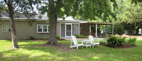 A house with a porch, two white chairs, and a lawn.