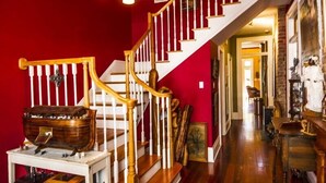 Una imponente escalera con balaustres blancos y barandilla de madera, que conduce a una habitación con pared roja y suelo de madera.