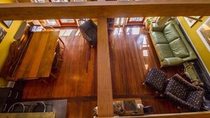 Una habitación amplia con piso de madera, un sofá verde y una zona de comedor con mesa y sillas de madera.