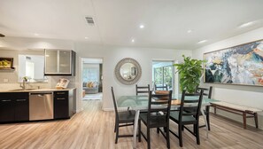 A modern kitchen with a dishwasher, a dining area with a glass table and chairs, and a large abstract painting on the wall. - ❤️ Charming Coastal Pool Home - 1 Mile to Siesta Key - Relax & Unwind (Sarasota)