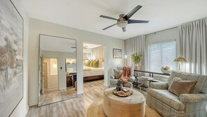 Uma sala de estar moderna com ventilador de teto, sofá, mesa de centro e uma cama ao fundo.