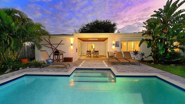 Área ao lado da piscina com piscina, espreguiçadeiras, mesa e cadeiras.