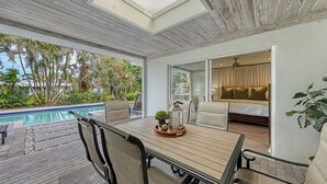 Uma área de refeições ao ar livre moderna com piscina, deck de madeira e vista para a piscina e vegetação.