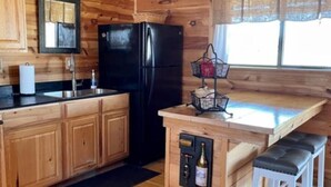 A wooden cabin kitchen with a black refrigerator, wooden cabinets, a sink, and a small bar area with stools.
