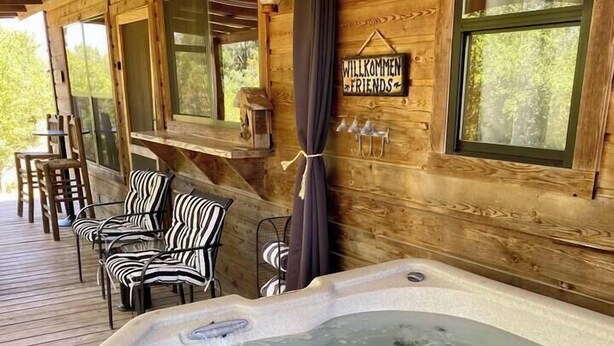 A wooden cabin with a hot tub, outdoor seating, and a welcome sign.