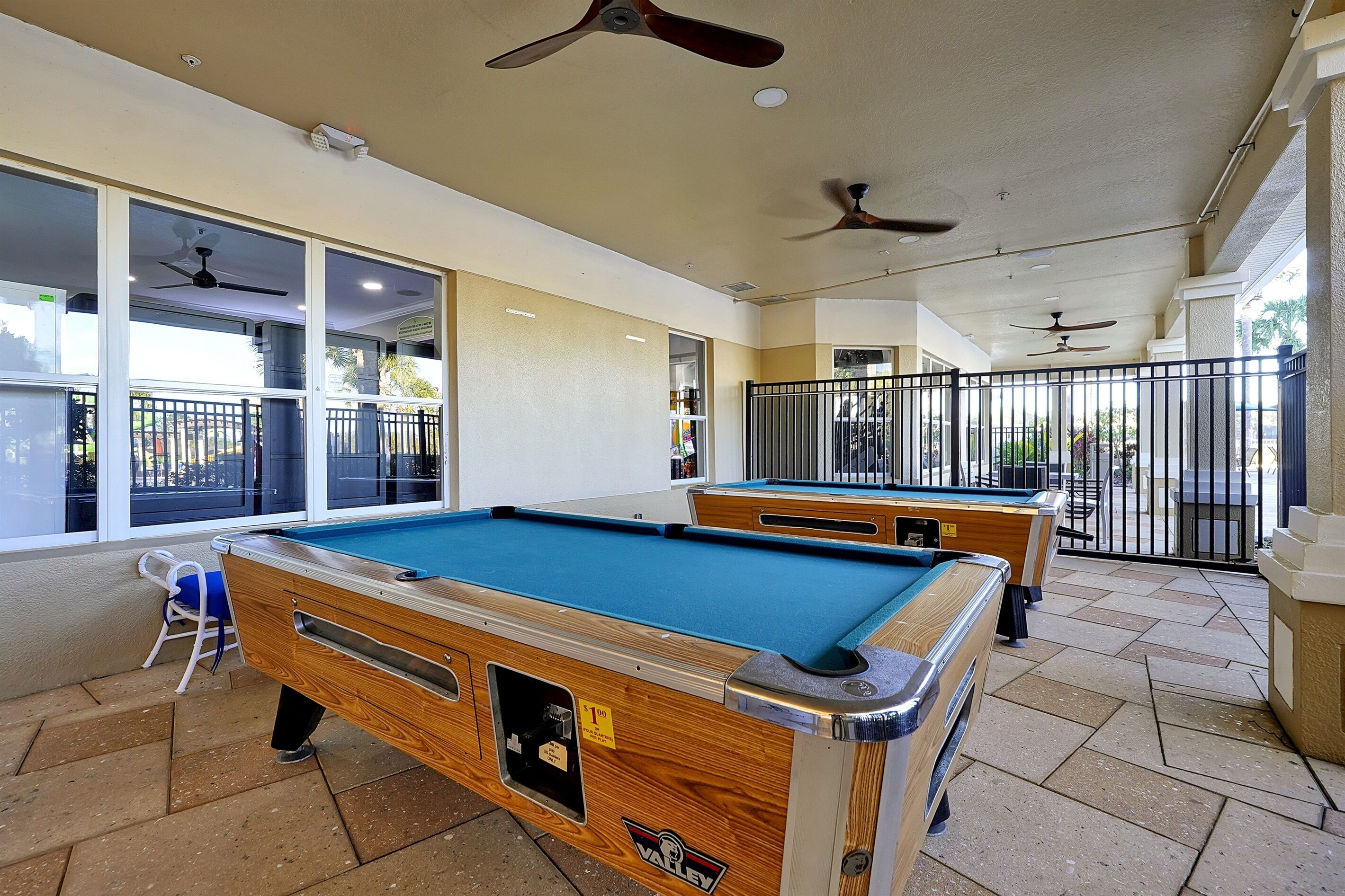 Un espace dédié aux tables de billard, équipé de ventilateurs de plafond, d’une table de billard et d’un coin salon avec des chaises.