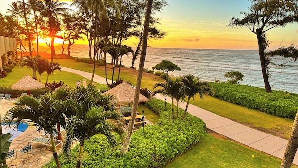 A resort with a pool, lounge chairs, and a pathway leading to the beach. - Direct Ocean Front, Top Floor Studio Paradise (Kapaa)
