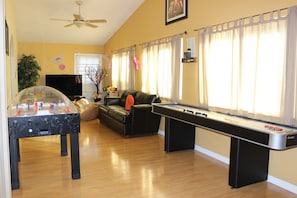 Una sala de estar con mesa de fútbol de mesa, mesa de billar, sofá y televisor.