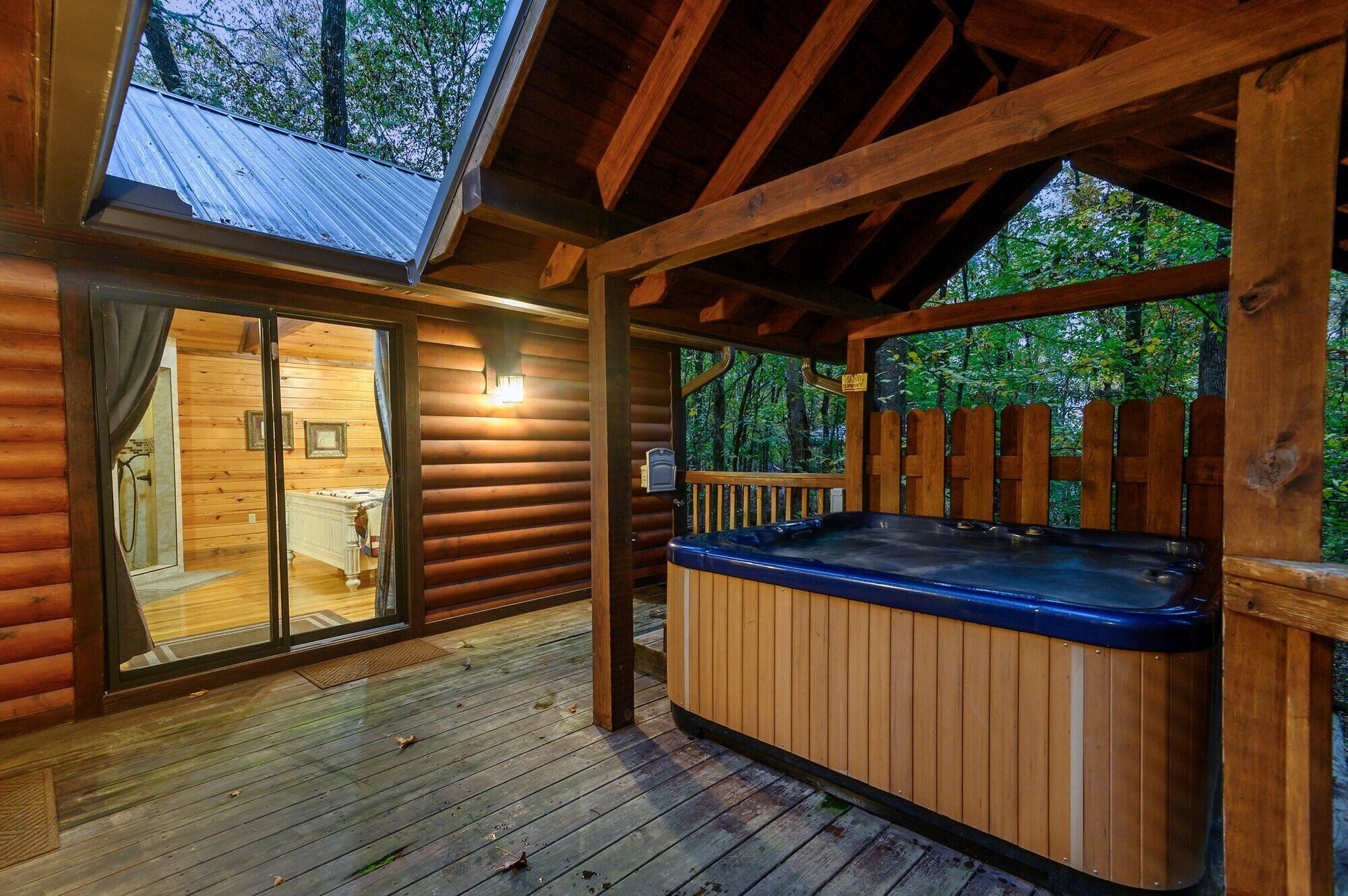 Een houten blokhut met een jacuzzi, een glazen deur naar een badkamer en een terras met uitzicht op een bos.