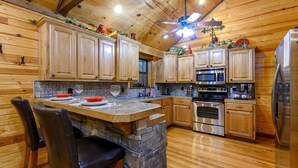 Una cocina tipo cabaña de madera con encimeras de piedra, armarios de madera y una isla de piedra con taburetes de bar.