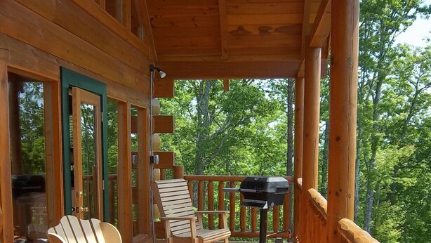 Una terraza de madera con sillas Adirondack y una parrilla, con vistas a un área boscosa.