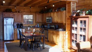 Interior de una cabaña de madera con cocina, comedor y un rincón de lectura.
