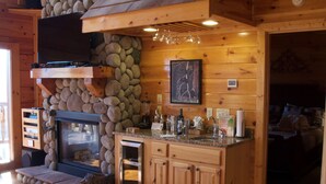 Interior acogedor de una cabaña con chimenea de piedra, armarios de madera y una zona de cocina.