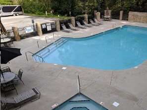 A swimming pool with lounge chairs and tables, surrounded by a fence and trees. - Romantic Luxury Getaway,Breathtaking View,Free HS WiFi,Htub,Xm,Smart Home Theatr (Pigeon Forge)