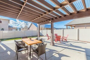 A covered patio area with a wooden table and wicker chairs, a pergola overhead, and a view of neighboring houses. - Juniper I: Fire Pit, Grill, and Bikes (Fruita)